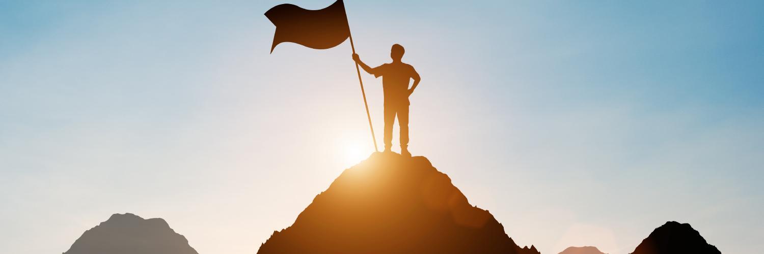 Figure on a hilltop holding flag with sun in the background