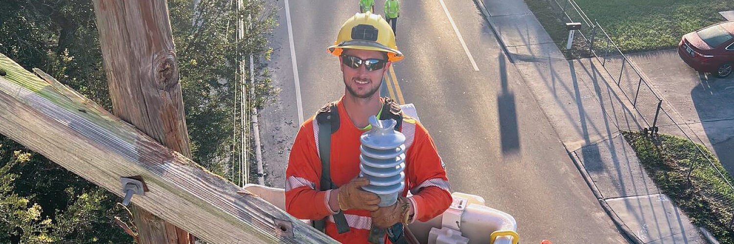 Lineworker in bucket truck next to utility pole holding equipment and smiling at camera