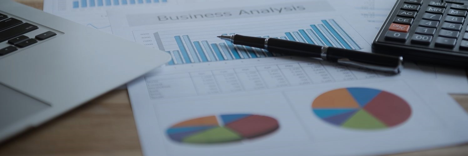 Pen and keyboard on top of document with graphs and charts