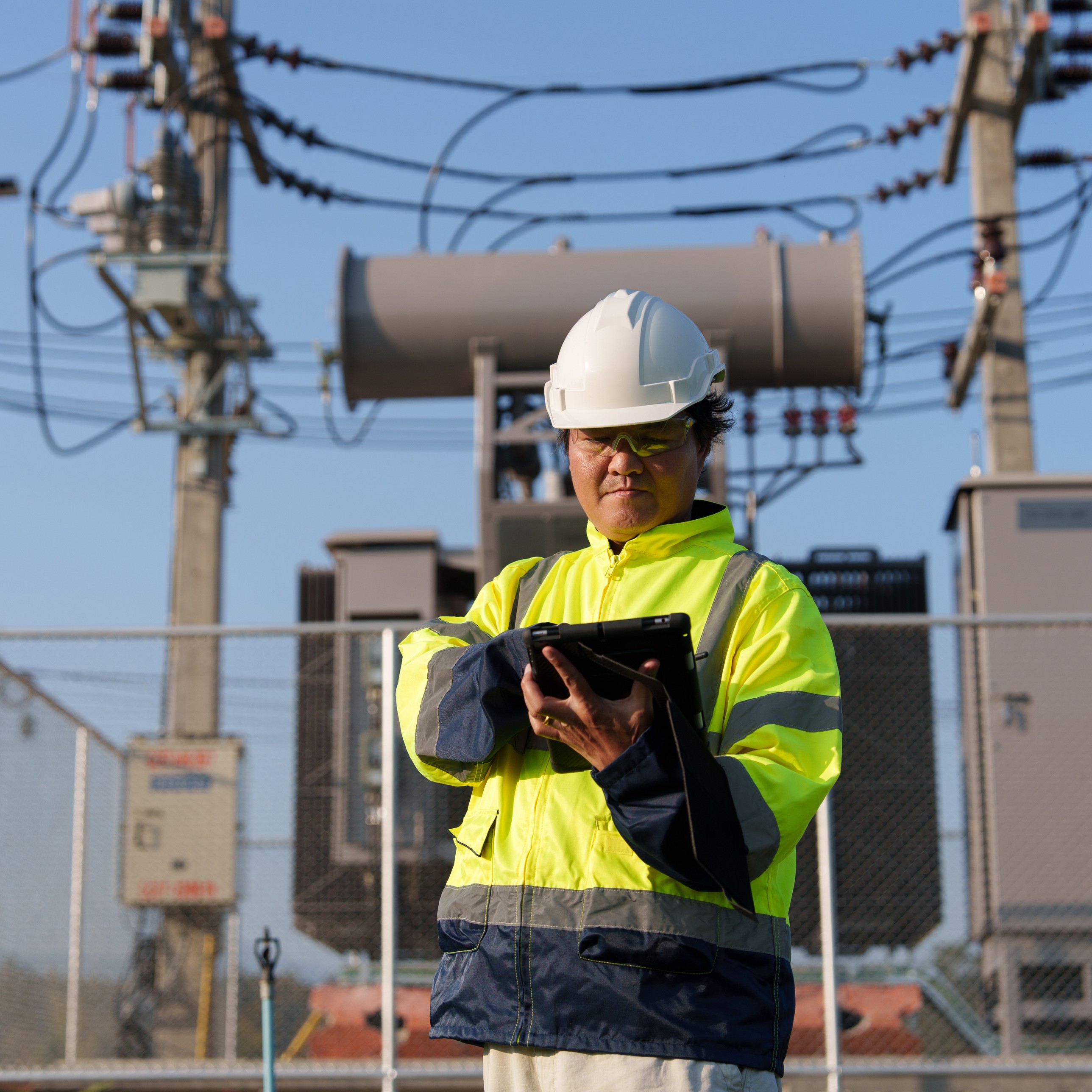 Utility worker with a tablet in front of a substation