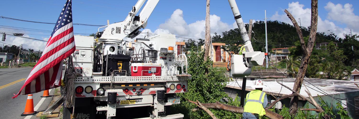 Utility truck with American flag parked next to fallen trees and damaged building