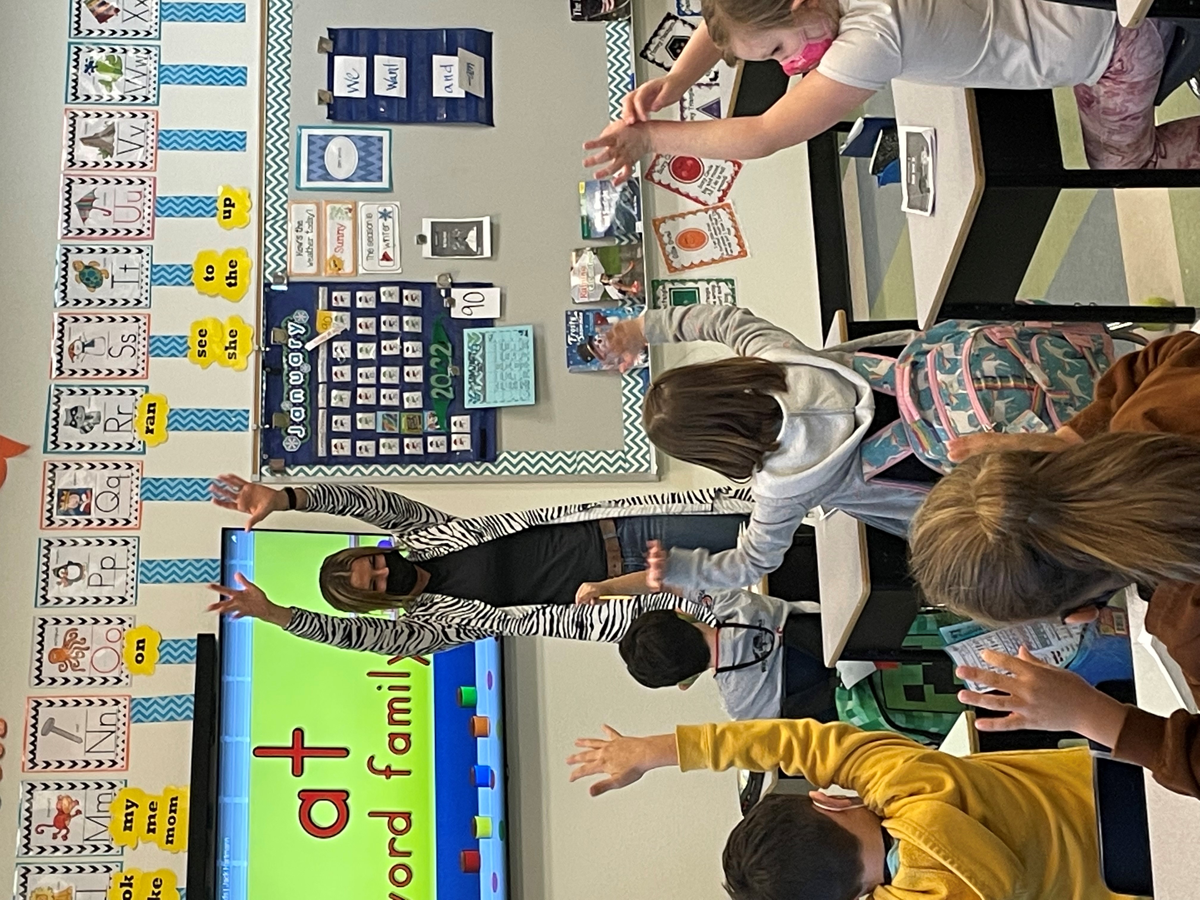 A teacher in the front of her classroom with her arms raised to signify a touchdown