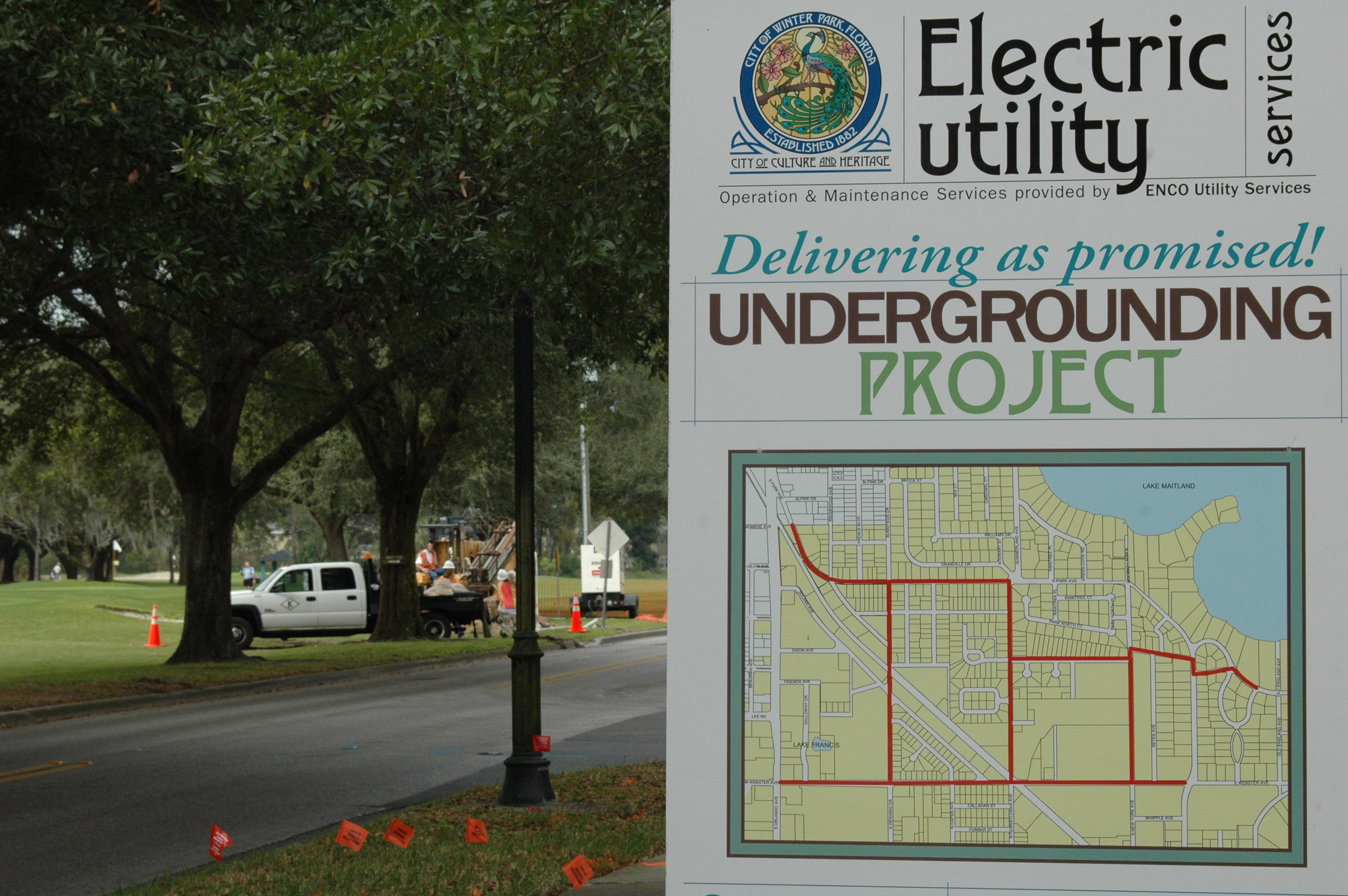 A Winter Park utility crew works on undergrounding behind a sign explaining the project. 