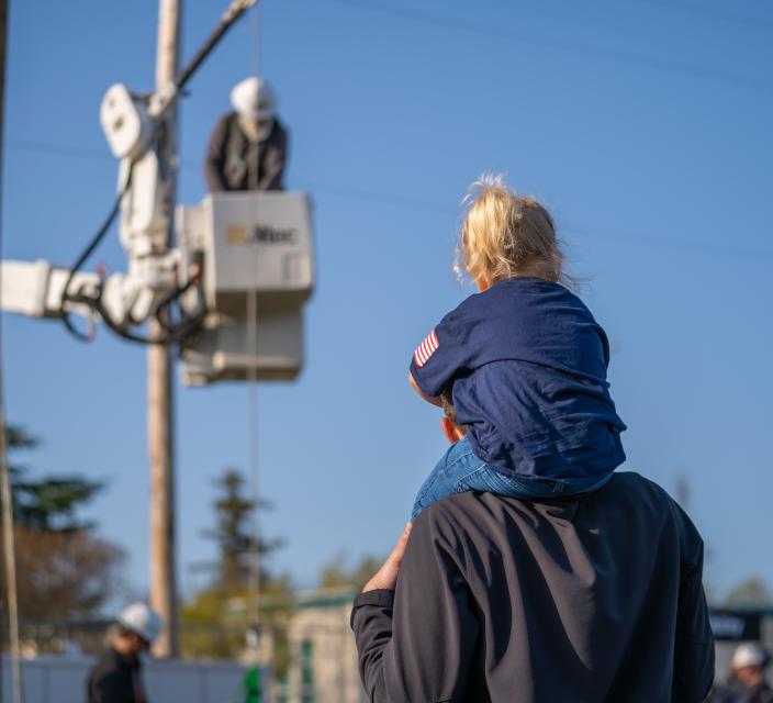 Child on shoulders watches lineworkers rodeo competition