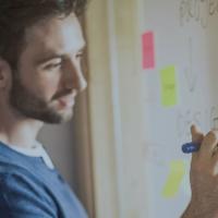 two people writing and looking at whiteboard