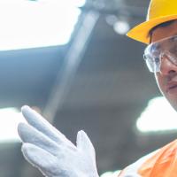A utility worker in a hardhat and orange vest putting on a white glove