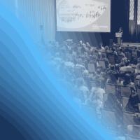 Black-and-white image of people in a large conference session with a blue graphic overlay