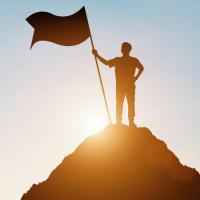 Silhouette of a person standing on a hilltop holding a flag