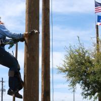 Rylee Gunn climbs a utility pole with the American flag in the background.