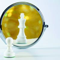 a chess pawn looking in the mirror at a reflection of a king piece