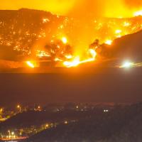 a wildfire burns through a valley in a night sky