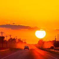 A truck driving down a road flanked by electric utility lines and transformers as the sun sets