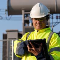 Electrical worker on a tablet in front of a substation