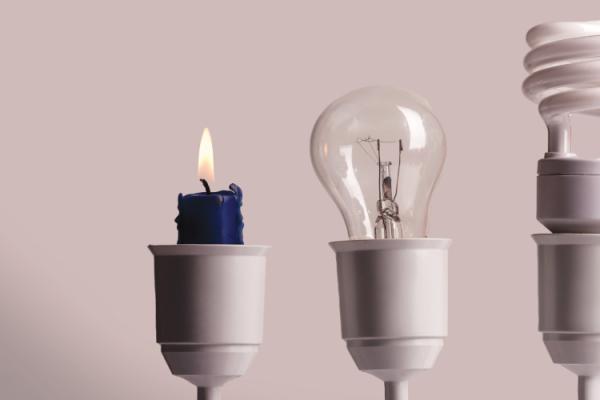 a candle and three types of light bulbs in a line, showing how light sources have evolved