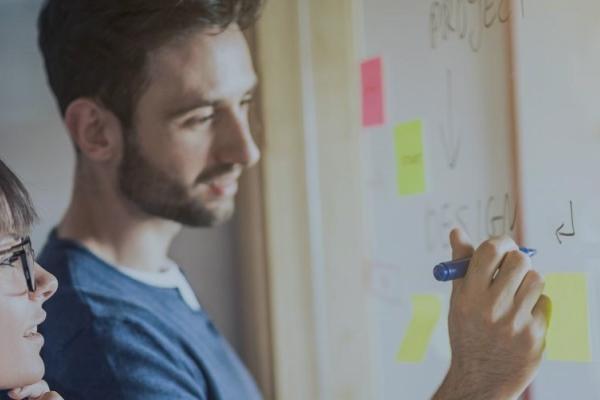 two people writing and looking at whiteboard