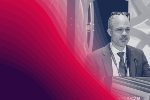 Black-and-white image of a person talking at a podium with a red graphic overlay