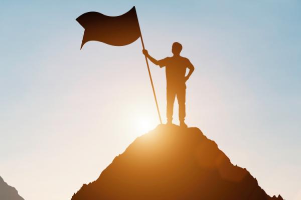 Silhouette of a person standing on a hilltop holding a flag