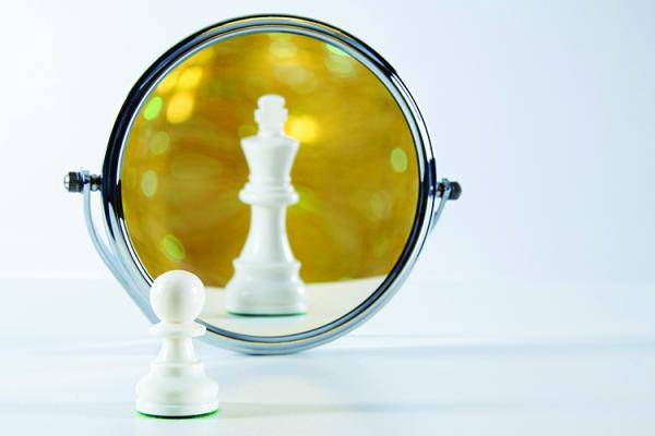 a chess pawn looking in the mirror at a reflection of a king piece
