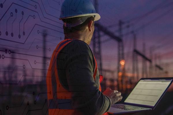 utility worker with laptop in front of a substation at dusk
