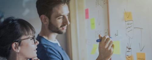 two people writing and looking at whiteboard