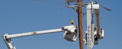 A lineworker in a bucket truck working on top of a utility pole