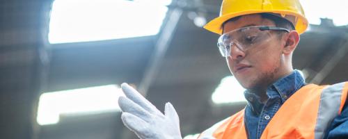A utility worker in a hardhat and orange vest putting on a white glove