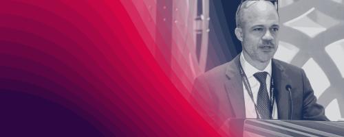 Black-and-white image of a person talking at a podium with a red graphic overlay