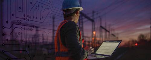 utility worker with laptop in front of a substation at dusk