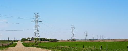Transmission towers over a field and dirt road - Heartland 