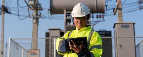 Electrical worker on a tablet in front of a substation